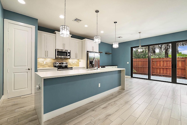 kitchen featuring pendant lighting, white cabinetry, appliances with stainless steel finishes, and an island with sink