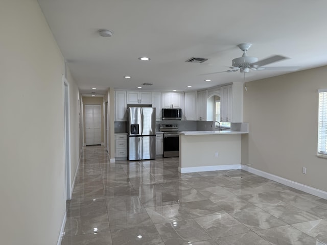 kitchen featuring kitchen peninsula, stainless steel appliances, ceiling fan, sink, and white cabinets