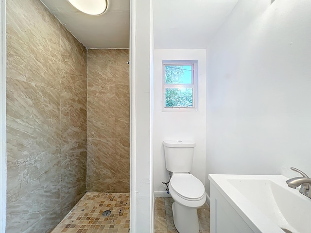 bathroom with a tile shower, vanity, and toilet