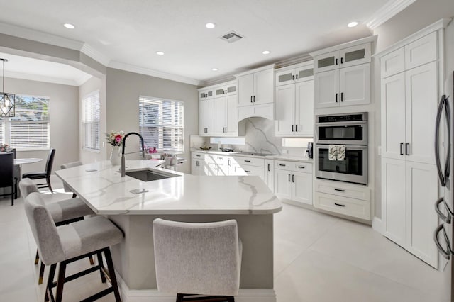 kitchen with a kitchen bar, a kitchen island with sink, sink, pendant lighting, and white cabinets