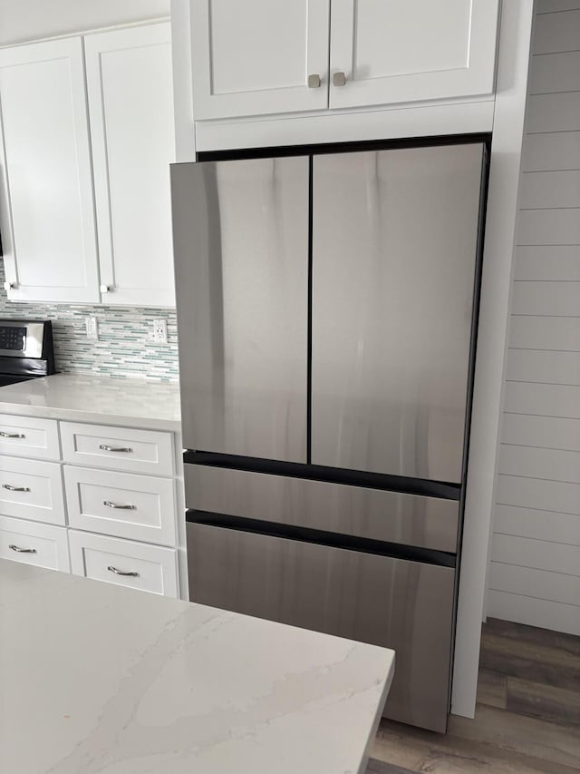 kitchen with wood-type flooring, light stone countertops, tasteful backsplash, white cabinetry, and stainless steel refrigerator