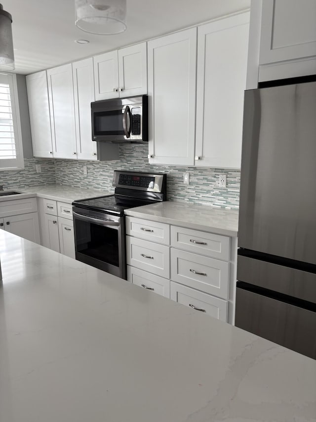 kitchen featuring light stone countertops, decorative backsplash, white cabinets, and stainless steel appliances