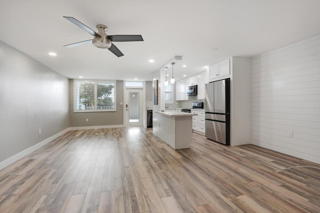 kitchen with a center island, stainless steel appliances, light countertops, open floor plan, and white cabinets