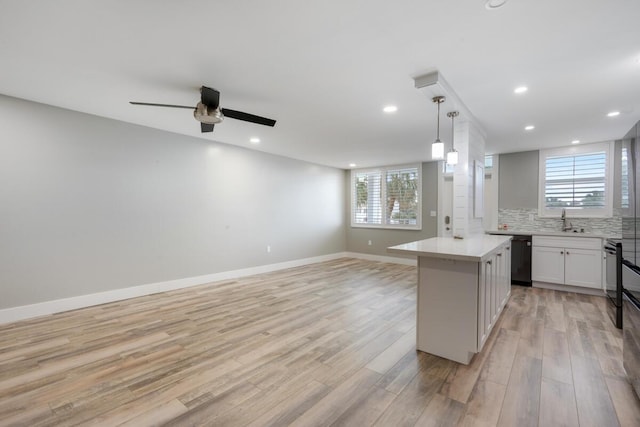 kitchen featuring light countertops, hanging light fixtures, white cabinets, a kitchen island, and a sink