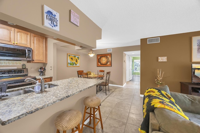 kitchen featuring a breakfast bar, sink, light stone countertops, light tile patterned flooring, and range