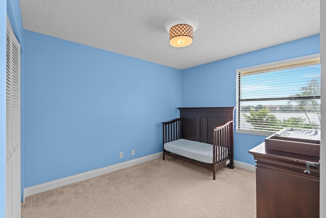 bedroom with a textured ceiling, light colored carpet, and a nursery area