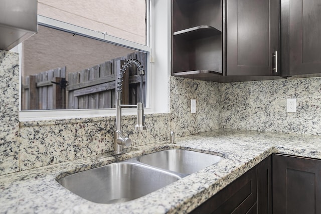 kitchen featuring dark brown cabinets, light stone countertops, sink, and tasteful backsplash