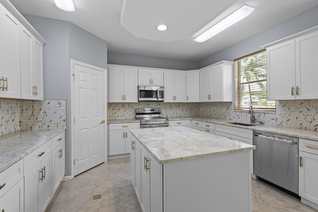 kitchen featuring light stone countertops, appliances with stainless steel finishes, a kitchen island, sink, and white cabinetry