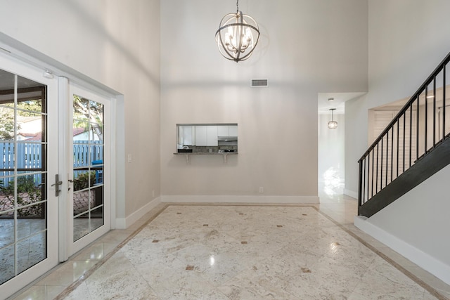 entryway featuring french doors, a towering ceiling, and a chandelier