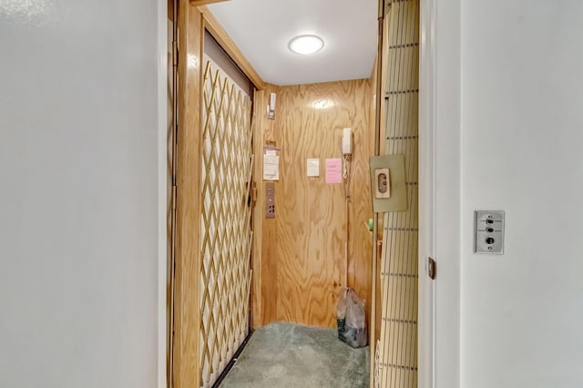 hall with carpet flooring, wood walls, and elevator