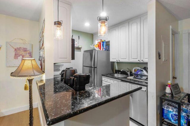 kitchen with white cabinetry, stainless steel appliances, light hardwood / wood-style flooring, dark stone counters, and decorative light fixtures