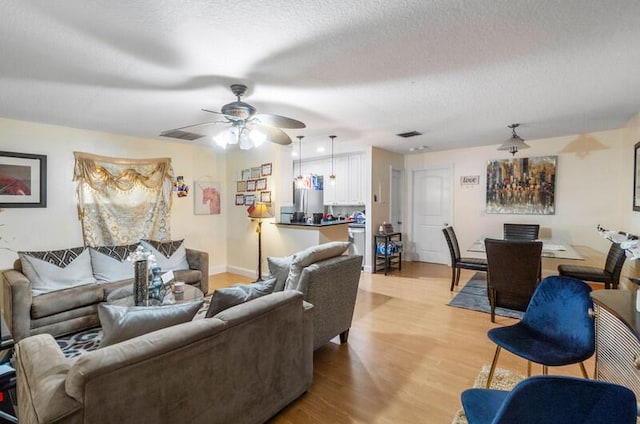 living room with ceiling fan, a textured ceiling, and light hardwood / wood-style flooring