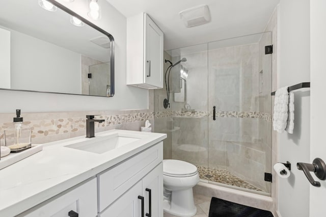 bathroom with vanity, a shower with door, tile patterned floors, toilet, and tile walls