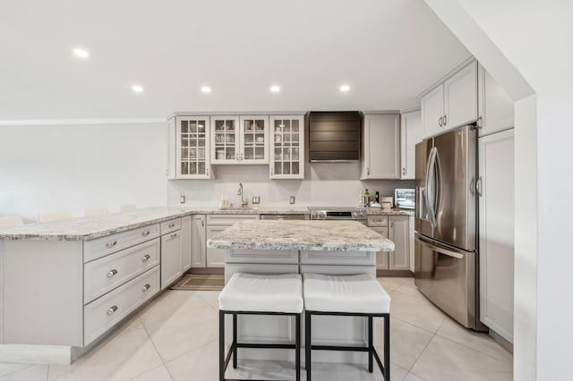 kitchen with a kitchen breakfast bar, stainless steel appliances, ventilation hood, sink, and a kitchen island