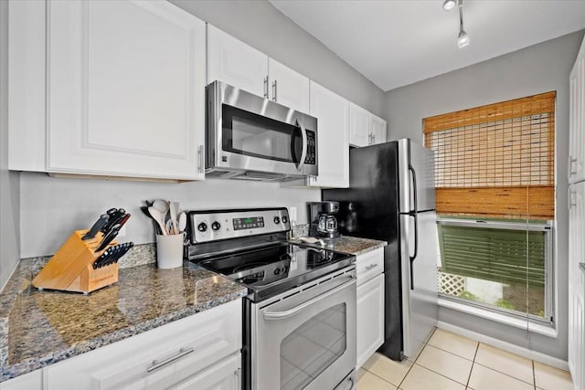 kitchen featuring stainless steel appliances, white cabinets, dark stone countertops, track lighting, and light tile patterned floors