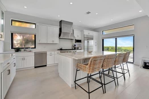 kitchen featuring wall chimney range hood, a kitchen island, a breakfast bar, white cabinetry, and appliances with stainless steel finishes