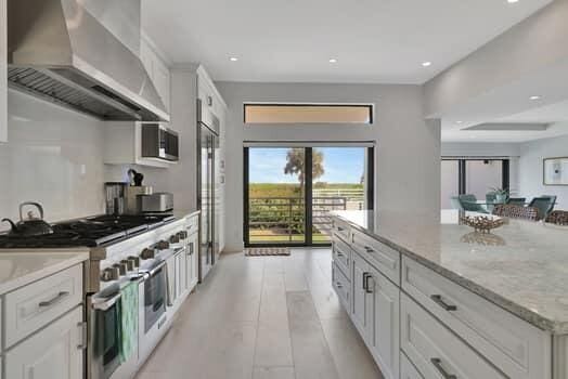 kitchen with light stone countertops, a center island, white cabinetry, wall chimney range hood, and stainless steel appliances