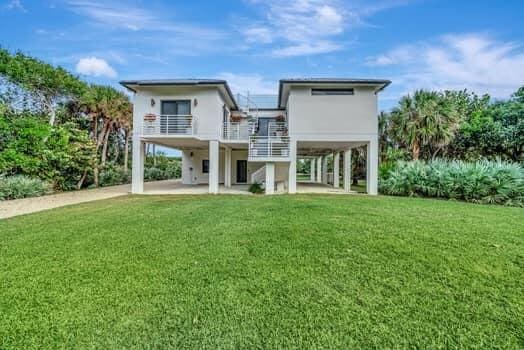 rear view of property with a carport, a balcony, and a yard