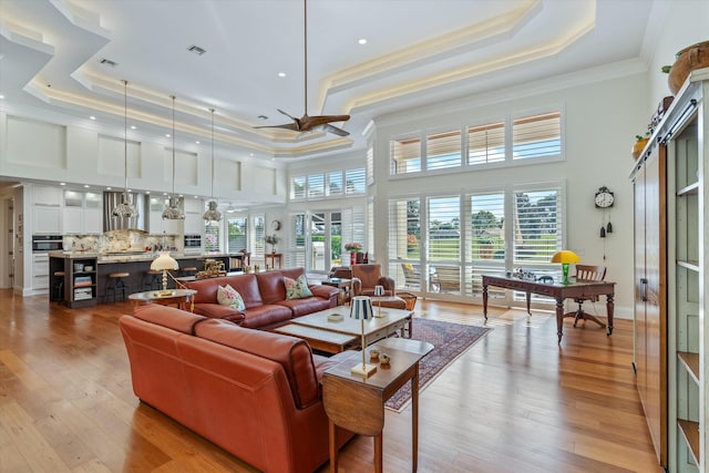 living room featuring a wealth of natural light, a tray ceiling, and light wood-style floors