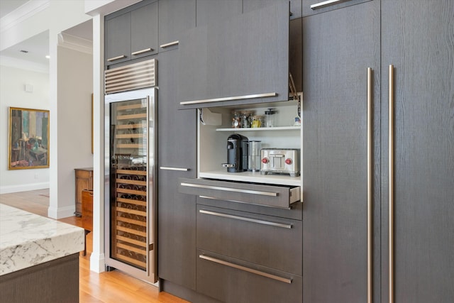 bar with light wood-type flooring, beverage cooler, baseboards, and crown molding