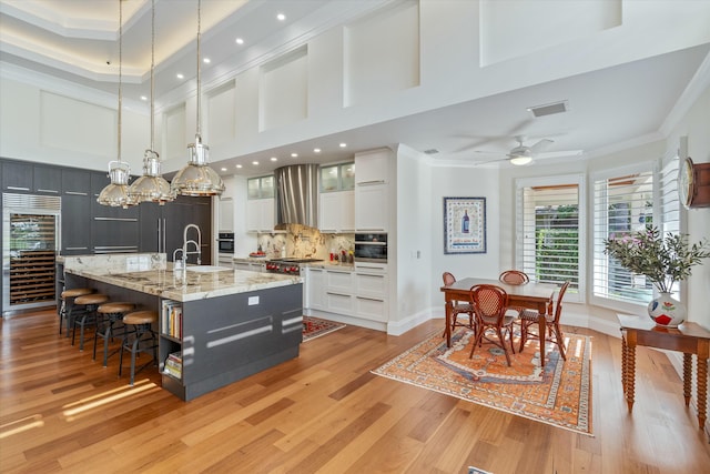 kitchen featuring pendant lighting, glass insert cabinets, white cabinets, a large island with sink, and wall chimney exhaust hood