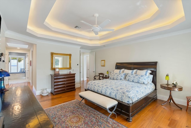 bedroom with a tray ceiling, wood finished floors, and visible vents