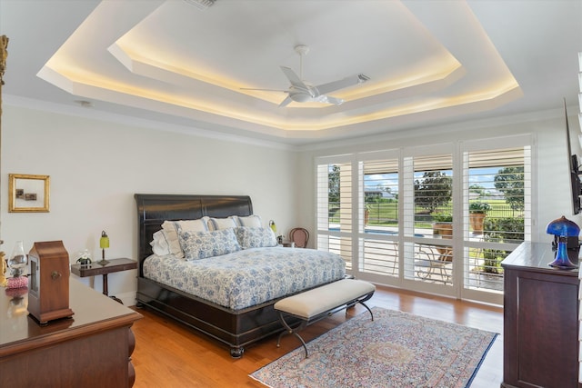 bedroom featuring light wood-style flooring, a tray ceiling, ceiling fan, and access to outside