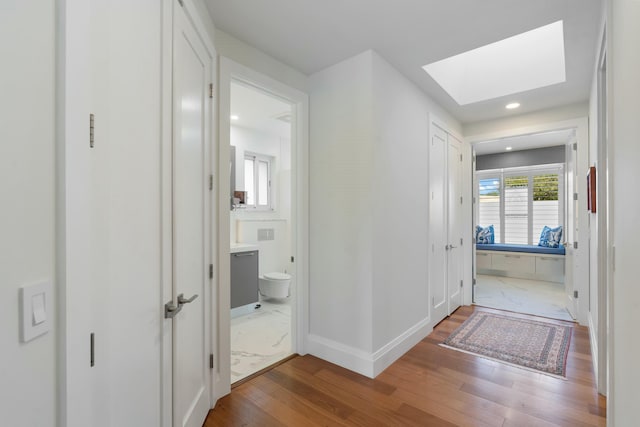 hall featuring a skylight, baseboards, wood finished floors, and recessed lighting