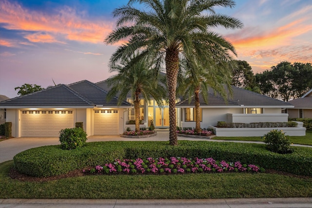 view of front of house with a tile roof, stucco siding, concrete driveway, a lawn, and a garage