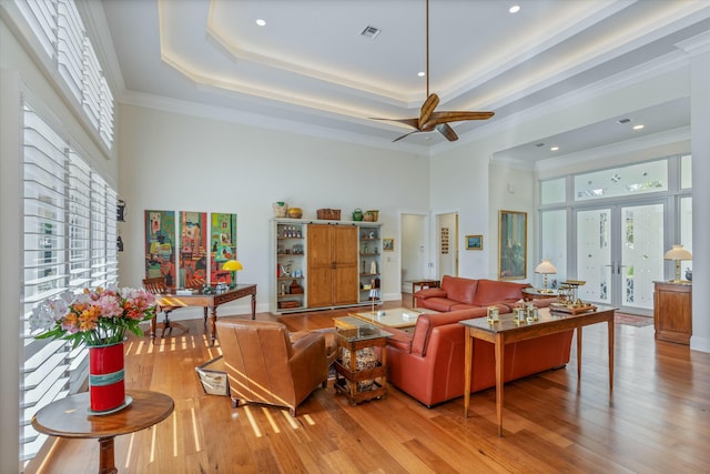 living room with light wood-style floors, a tray ceiling, french doors, and plenty of natural light