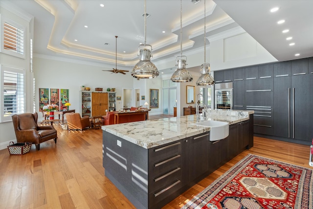 kitchen with a large island, open floor plan, decorative light fixtures, a tray ceiling, and a sink