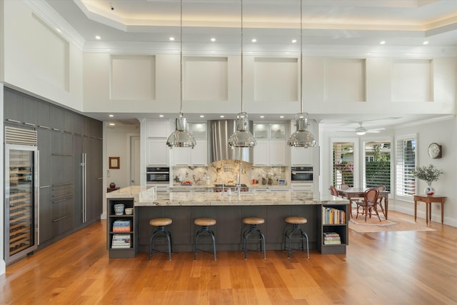 kitchen featuring wall oven, white cabinets, glass insert cabinets, decorative light fixtures, and light stone countertops