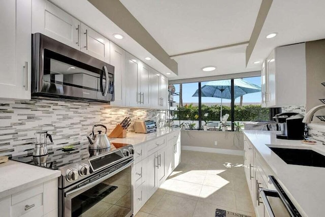 kitchen featuring white cabinetry, sink, tasteful backsplash, light tile patterned flooring, and appliances with stainless steel finishes