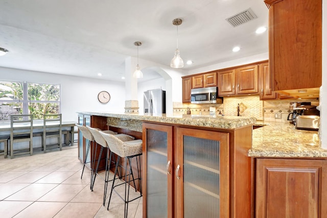 kitchen featuring a kitchen bar, appliances with stainless steel finishes, kitchen peninsula, light tile patterned floors, and decorative light fixtures