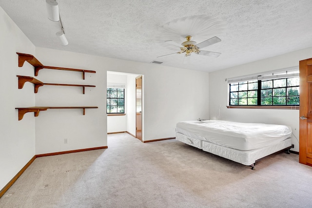 unfurnished bedroom with ceiling fan, rail lighting, light carpet, and a textured ceiling