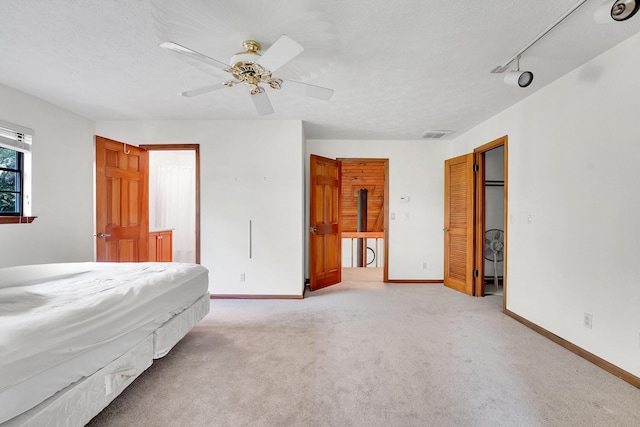 unfurnished bedroom featuring ceiling fan, rail lighting, light colored carpet, and a textured ceiling