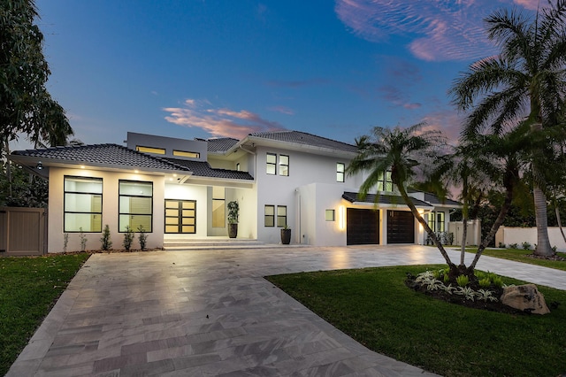 view of front of home featuring driveway, a tiled roof, an attached garage, fence, and stucco siding