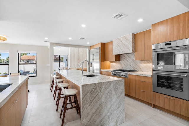 kitchen featuring a kitchen breakfast bar, stainless steel appliances, sink, an island with sink, and range hood