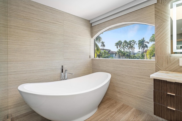 bathroom featuring vanity, a tub to relax in, and tile walls