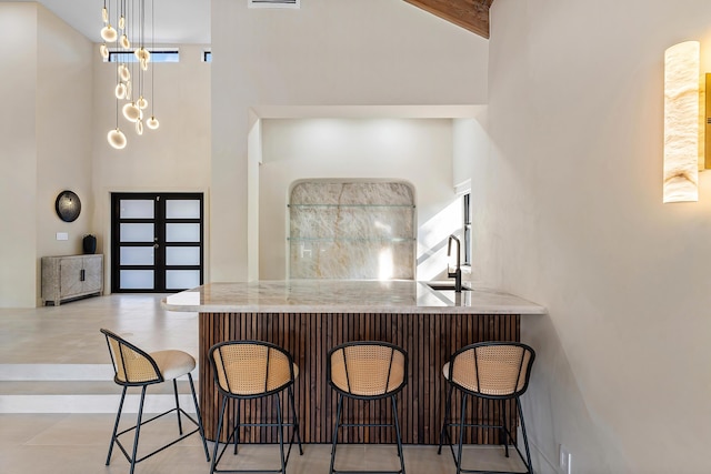 kitchen featuring kitchen peninsula, a breakfast bar, decorative light fixtures, beamed ceiling, and a high ceiling