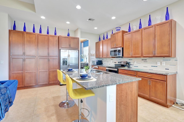 kitchen with a kitchen bar, a kitchen island with sink, sink, light stone counters, and stainless steel appliances