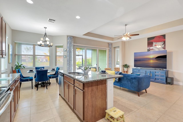 kitchen featuring dishwasher, light stone counters, a kitchen island with sink, light tile patterned floors, and range