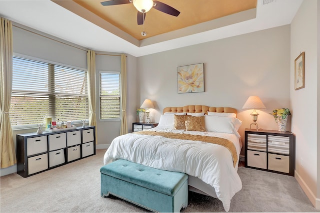 bedroom with light carpet, a tray ceiling, and ceiling fan