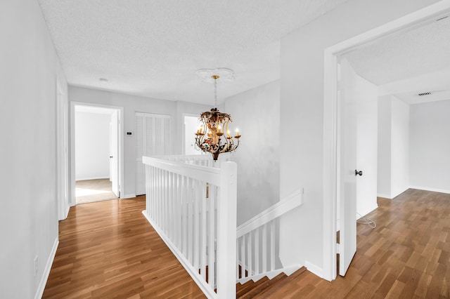 corridor featuring wood-type flooring, a textured ceiling, and a notable chandelier