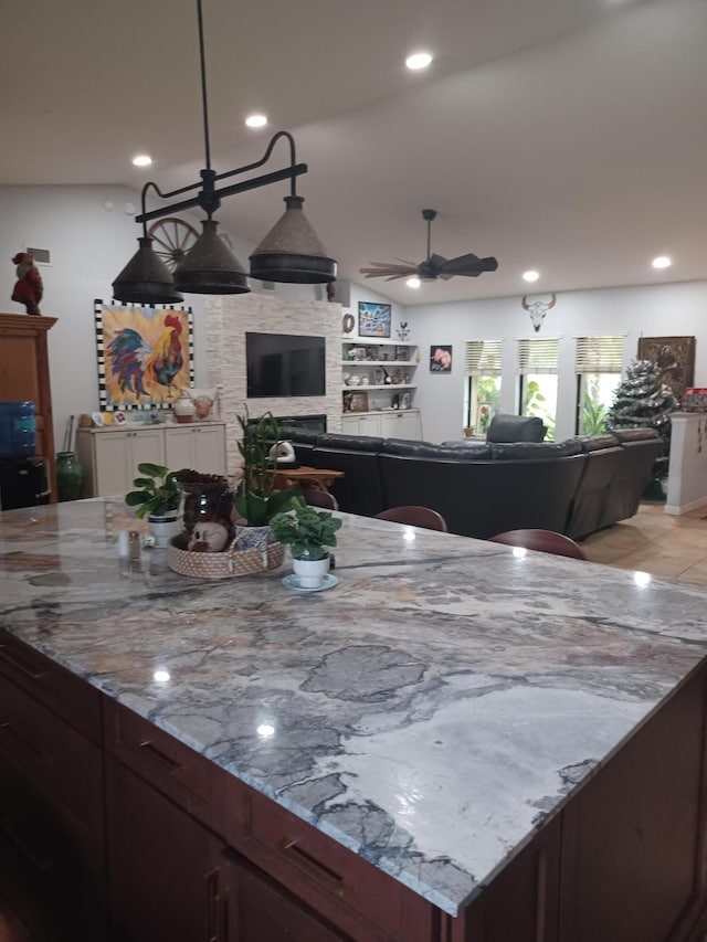 kitchen featuring a fireplace, ceiling fan, built in features, and light stone counters