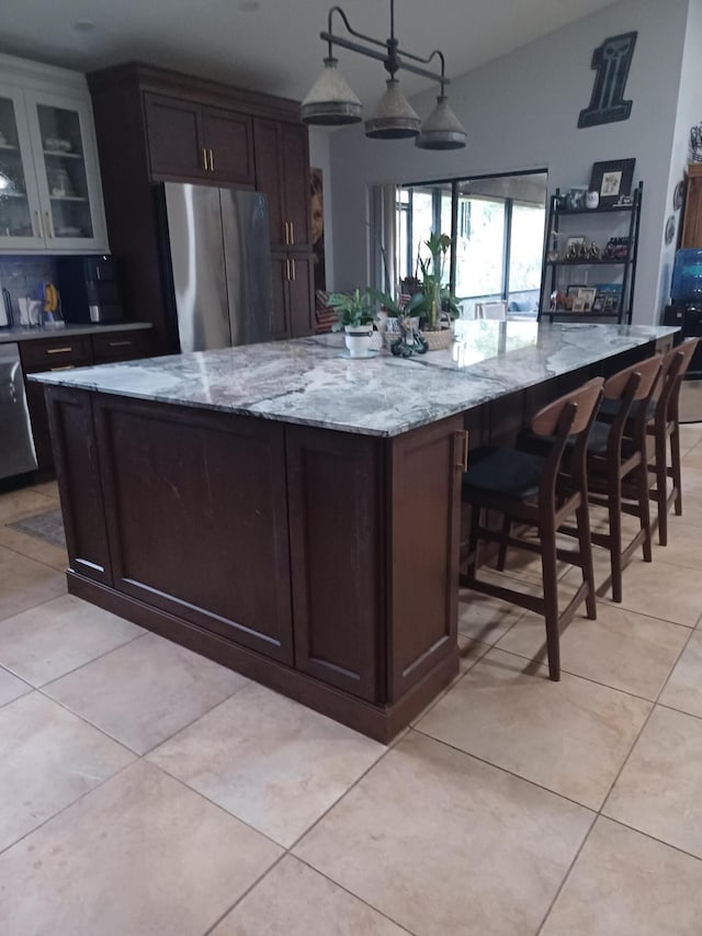 kitchen featuring appliances with stainless steel finishes, dark brown cabinets, light stone counters, and hanging light fixtures