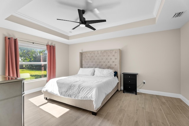 bedroom with light wood-type flooring, a raised ceiling, ceiling fan, and ornamental molding