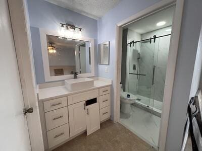 bathroom with ceiling fan, walk in shower, a textured ceiling, toilet, and vanity