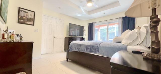 bedroom featuring light tile patterned floors, a closet, a raised ceiling, and ceiling fan