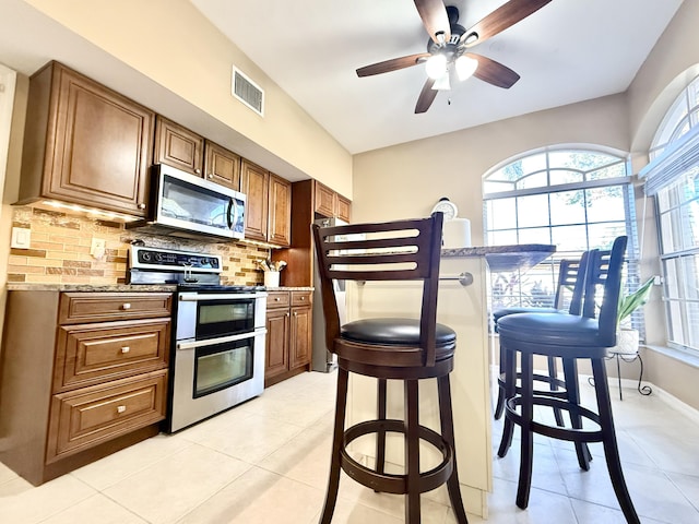 kitchen with decorative backsplash, light stone counters, appliances with stainless steel finishes, light tile patterned flooring, and a kitchen bar